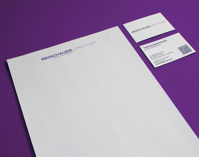 Eine klassische Geschäftsausstattung besteht aus Briefbogen und Visitenkarten, einheitlich gestaltet mit dem Logo. Beides liegt hier zu sehen auf einem violett farbigen Hintergrund.