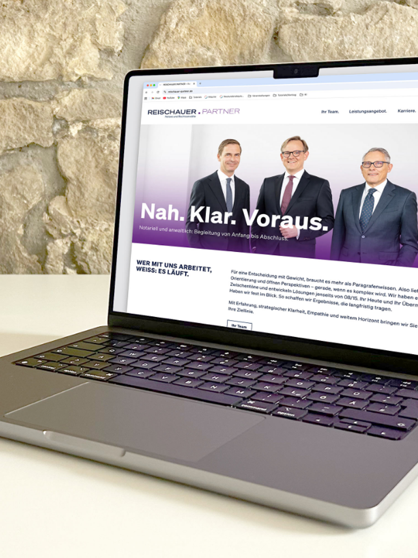 Die Startseite der Webseite Reischauer und Partner ist auf dem Bildschirm des MacBooks zu sehen. Das Laptop steht auf einen weißen Tische im Hintergrund ist eine unverputzte Wand zu sehen.