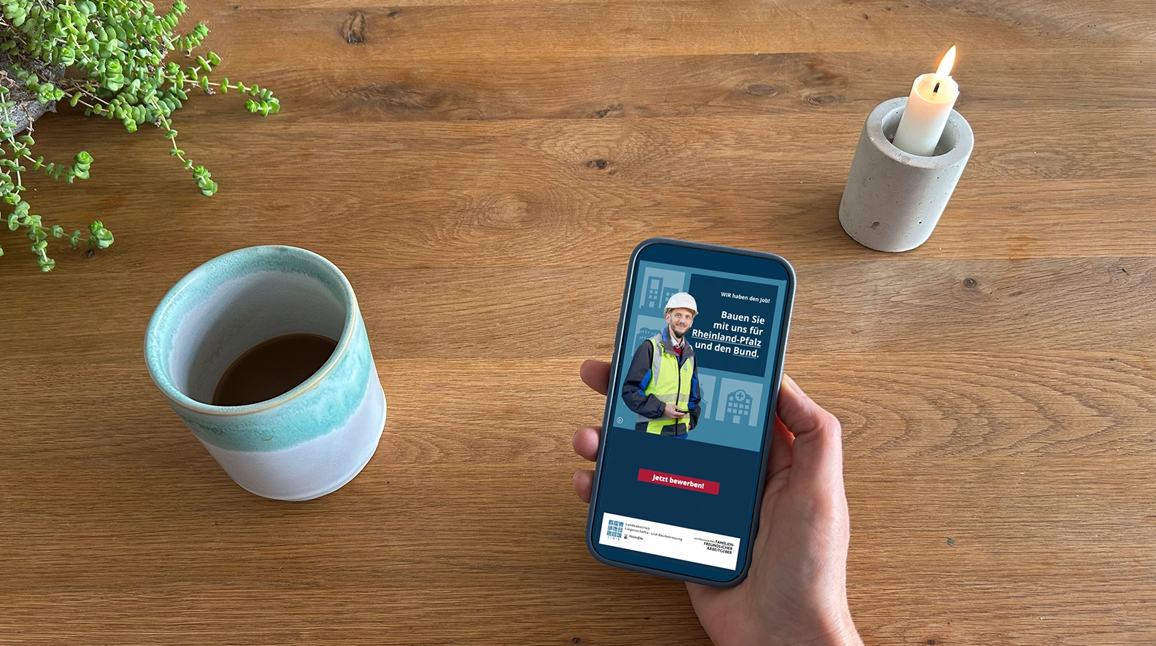 Handy wird in der Hand gehalten im Hintergrund ist ein Holztische, eine Tasse Kaffee, eine Kerze und eine Grünpflanze zu sehen. Im Display wird die InApp Werbung gezeigt.