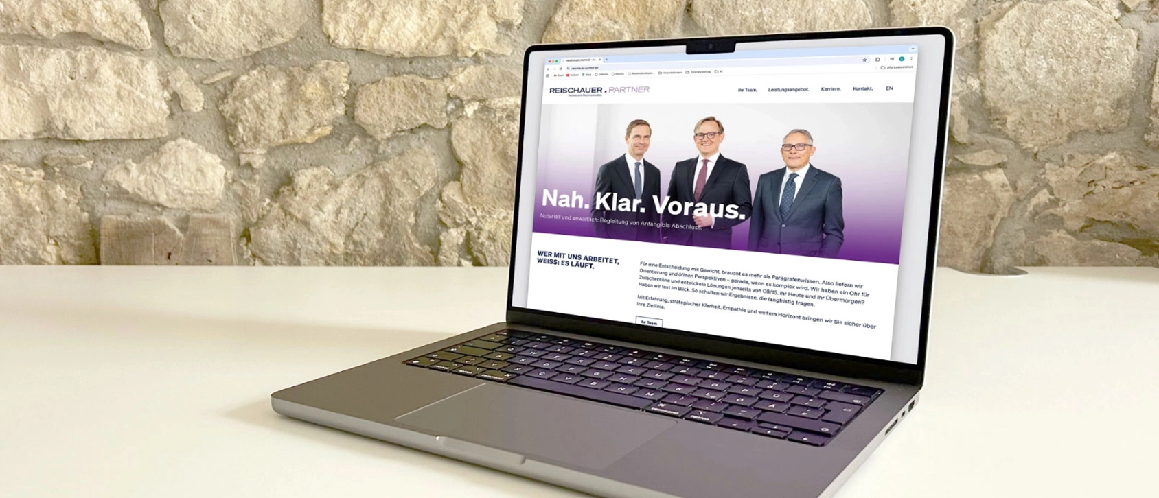Die Startseite der Webseite Reischauer und Partner ist auf dem Bildschirm des MacBooks zu sehen. Das Laptop steht auf einen weißen Tische im Hintergrund ist eine unverputzte Wand zu sehen.